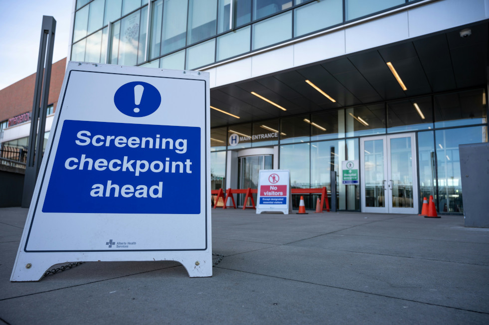 Hospital entrance with a sign reading "Screening checkpoint ahead"